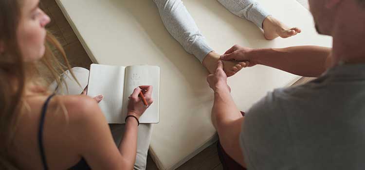hands of masseuse on patient's feet as observer takes notes