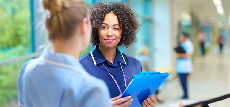 female CNA holding clipboard talking with nurse