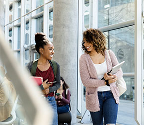 two students chatting in windowed hallway