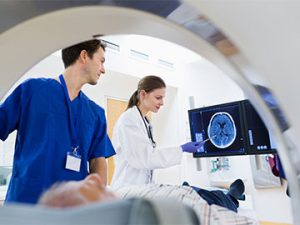 two medical staff look at brain scan of patient laying down