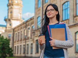 female student holding folders and coffee and walking by hospital