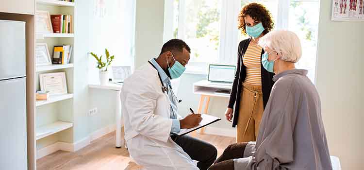 epidemiologist writing notes while talking with elderly patient and her daughter