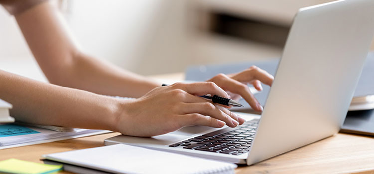 hands holding pen typing on laptop