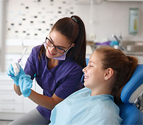 dental assistant shows young client the correct way to brush her teeth