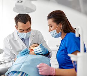 dental assistant helps dentist as he examines young patients teeth