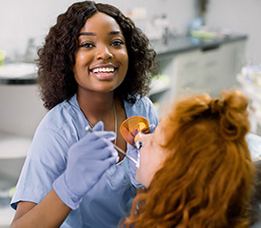 new jersey dental assistant smiling while she puts fluoride treatment on girls teeth