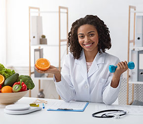 a sports nutritionist smiling at the camera holds an orange in one hand and a weight in the other