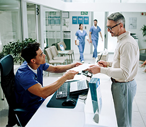 male medical assistant receives filled in paperwork from new patient in busy clinic