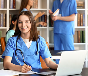 a medical assistant student works on her laptop in a library and smiles at the camera
