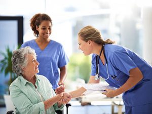 a medical assistant greets and shakes hands with a patient in a wheelchair