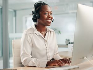 medical billers smiles while talking on phone headset and computer