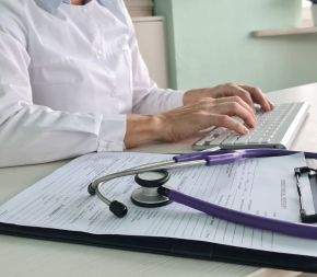 a healthcare professional uses a clipboard of doctors' notes to code procedures on a keyboard